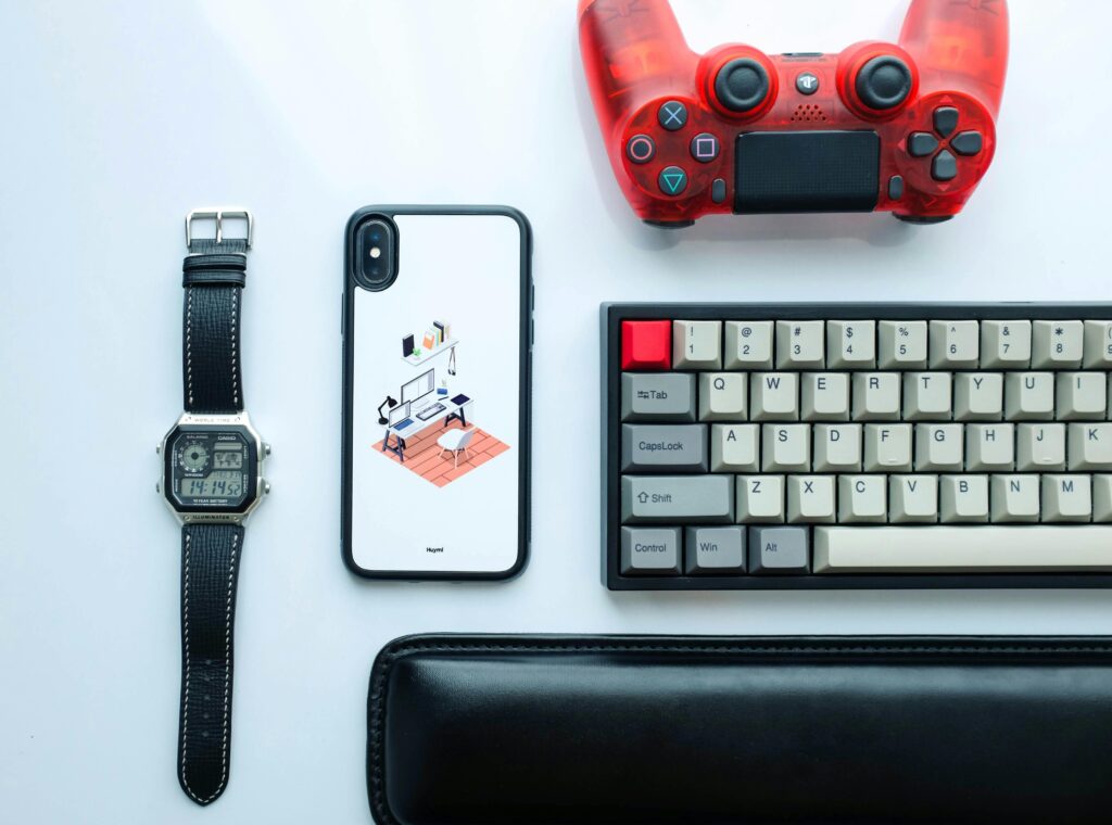 Top view of modern gadgets including a smartphone, watch, game controller, and keyboard.